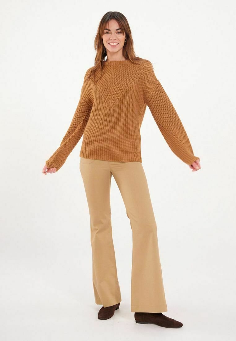Pull en tricot marron avec un motif en V, manches longues, associé à un pantalon beige évasé et des bottines marron. Texture lisse, coupe décontractée.
