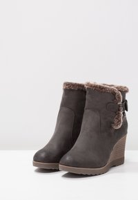 Stivali ankle in suede grigio con tacco a wedge, caratterizzati da un bordo in finta pelliccia nella parte superiore, un accento con fibbia laterale e suola in gomma testurizzata.