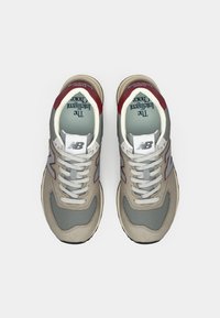 Sneaker beige e grigie con tomaia in mesh e scamosciato, linguetta in maglia, accenti rossi, lacci bianchi e suola testurizzata. Presenta il logo "NB".