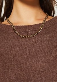 Guldhalsband ligger på en brunstickad tröja med ribbad halsringning. Kedjan har tjocka, sammanlänkade länkar.