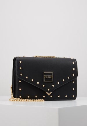 Bolso de hombro de cuero negro con acentos de tachuelas doradas, correa de cadena y cierre magnético. Presenta una placa con el logo de la marca en la parte frontal.