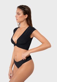 Crni bikini set koji se sastoji od topa s dubokim V-izrezom i detaljem u obliku zavrtnja s kratkim rukavima, uparen s odgovarajućim donjim dijelom bikinija s niskim strukom. Glatka tekstura.