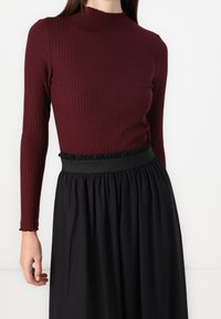 Ribbad bordeaux långärmad tröja parat med en svart kjol med ett rynkat midjeband. Den övergripande designen är åtsittande upptill med en utfläkt nederdel.