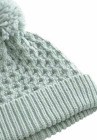 Berretto lavorato a maglia di colore verde chiaro con un motivo testurizzato, dotato di una fascia a coste e un pom-pom soffice nella parte superiore.