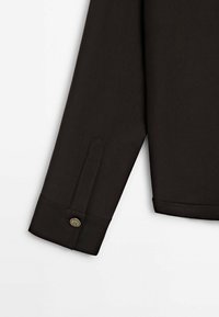 Manica di camicia marrone scuro con polsino bottonato, caratterizzata da un taglio dritto, una texture liscia e una leggera lucentezza.