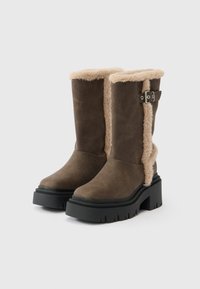 Barna szarvasbőr bokacsizma műszőrme béléssel, tömzsi fekete gumitalppal és oldalt csatos részlettel. Sima textúrával és masszív kialakítással bír.