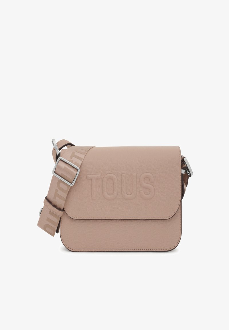 Bolso bandolera sintético beige con logo "TOUS" en relieve. Cuenta con cierre tipo solapa, correa ajustable y detalles en acero inoxidable.