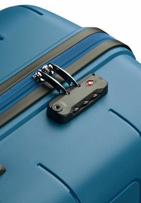 Maleta dura azul con superficie texturizada, cremalleras dobles y un candado aprobado por la TSA de color negro con emblema rojo, que cuenta con tres diales de combinación.