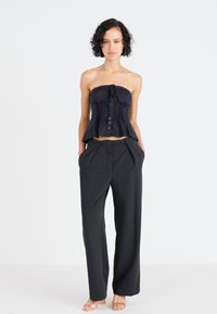 Μαύρο strapless τοπ με πτυχώσεις και κουμπιά, συνδυασμένο με ψηλόμεσες μαύρες παντελόνες με χαλαρή εφαρμογή και πλαϊνές τσέπες.