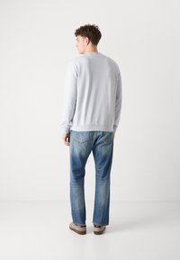 Sudadera azul clara de manga larga, con cuello redondo y dobladillo acanalado, combinada con jeans azules desgastados y zapatos marrones tipo slip-on.