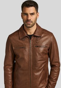 Chaqueta de cuero marrón con cuello de solapa, dos bolsillos en el pecho con cremallera y bolsillos laterales. Textura suave, diseño ajustado.