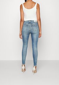 Fitted ljusblå denimjeans med hög midja, bakfickor och subtila slitningar, kombinerat med en vit ärmlös topp och klackar.