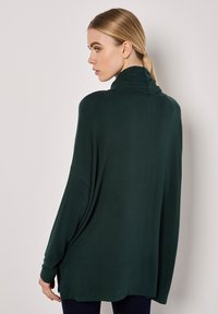 Tmavě zelený oversized rolák s dlouhými rukávy, vyrobený z měkké, lehké tkaniny, s designem zvlněného zadního dílu a uvolněným střihem.