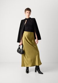 Black sleeveless top, olive green satin maxi skirt, fitted black blazer, black handbag with silver accents, and pointed black ankle boots.