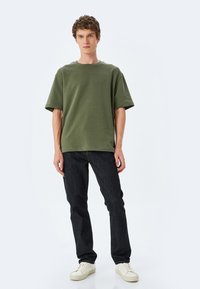 Oliven grøn kortærmet T-shirt med en afslappet pasform. Sammen med mørkeblå denim-jeans og hvide sneakers. Simpelt design, ingen synlige mønstre.