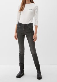 Jean skinny en denim gris foncé, avec une fermeture à bouton, cinq poches et un léger délavage. Associé à un haut à manches longues en côte blanc.