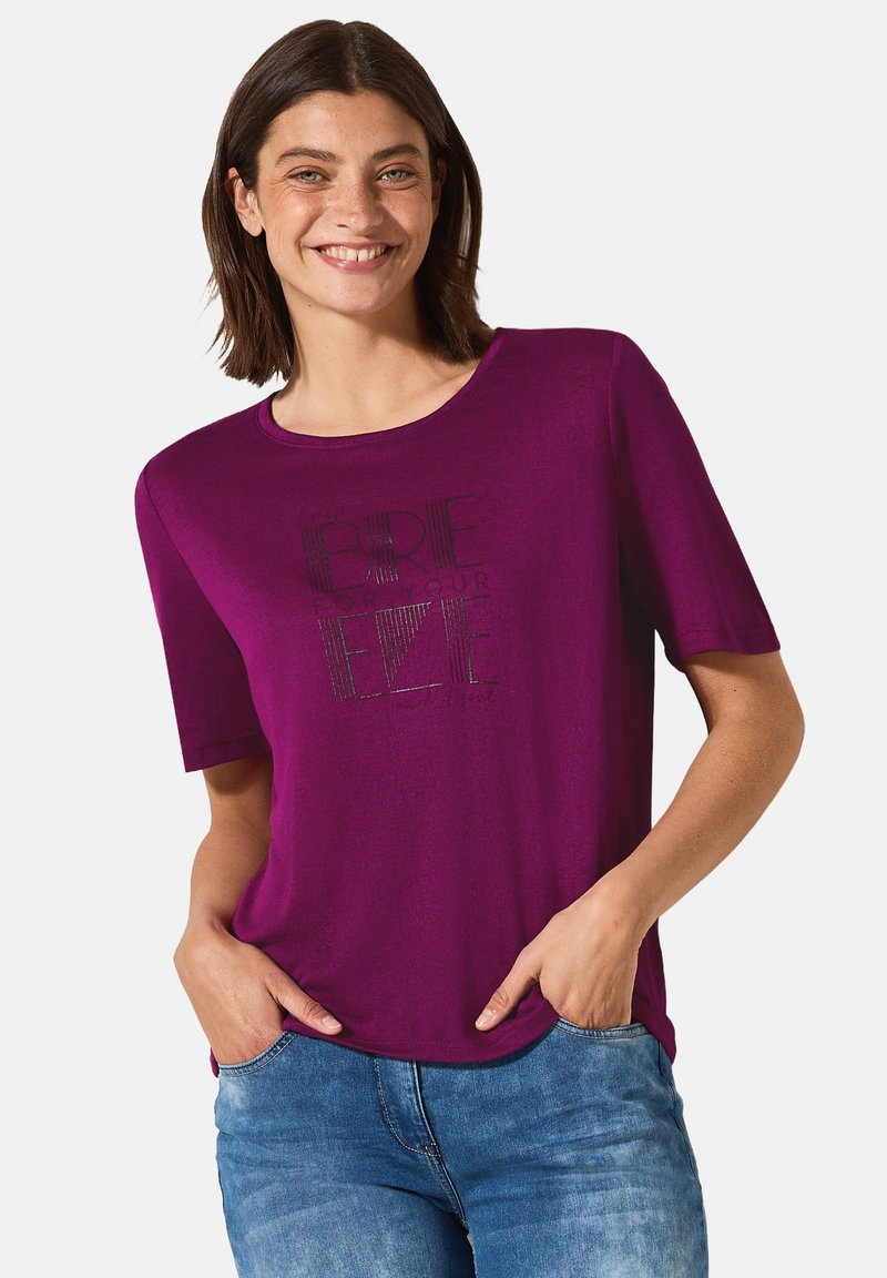 T-shirt à manches courtes violet en tissu doux, avec un design graphique en texte noir. Le col est rond et la coupe est décontractée.