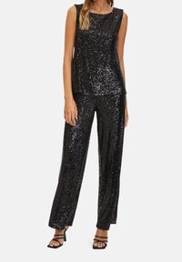 Svart paljettbeströdd ärmlös topp och vida byxor i set, med en slät textur och en glansig finish, kombinerat med svarta klackar med remmar.