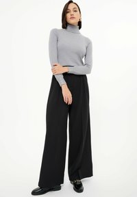 Jersey de cuello alto gris ajustado con mangas largas y acentos de botones, combinado con pantalones negros de cintura alta y pernera ancha, y zapatos brillantes.