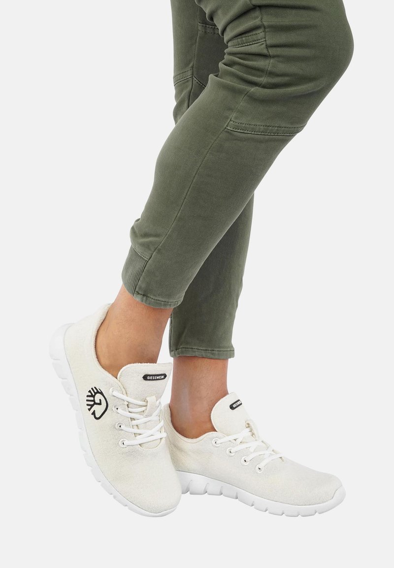 Helle beige Canvas-Sneaker mit weißen Gummisohlen. Zu den Merkmalen gehören eine runde Zehenpartie, ein Schnürdesign und ein Logo an der Seite.