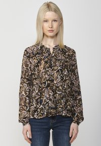 Blusa nera a fantasia con design paisley multicolore e dettagli in volant lungo il collo, abbinata a jeans blu aderenti.