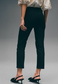 Jeans negros de cintura alta con un ajuste slim, que presentan una textura suave y detalles sutiles en los bolsillos. Combinados con tacones negros de tipo slingback con punta.