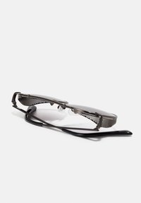 Saulesbrilles ar melnu rāmjiem, taisnstūra lēcām, sietveida akcentiem uz deguna tilta un elegantiem rokām. Teksturēti elementi piešķir vizuālu pievilcību.