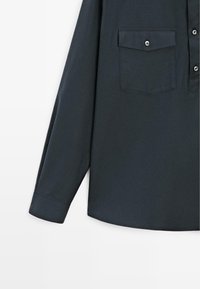 Donkerblauw overhemd met lange mouwen, voorzien van een knoopsluiting, twee borstzakken en manchetten met knopen. Gemaakt van gladde stof met een matte afwerking.