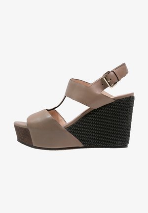 Sandalía de cuña de cuero beige con diseño recortado y correa ajustable en el tobillo. Presenta una plataforma tejida negra texturizada y un detalle de tacón de madera.