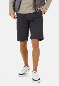 Shorts en tissu bleu marine avec poches latérales, une coupe décontractée et une surface texturée subtile, associés à des baskets blanches et bleu marine.