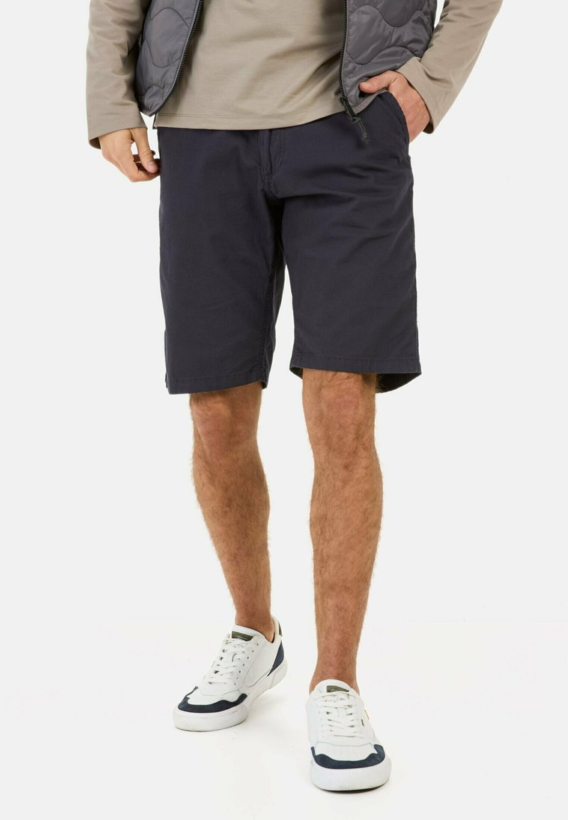 Shorts en tissu bleu marine avec poches latérales, une coupe décontractée et une surface texturée subtile, associés à des baskets blanches et bleu marine.