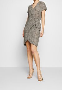 Robe portefeuille en tissu texturé et à motifs, avec un décolleté en V et des manches courtes. Schéma de couleurs gris et noir avec un ourlet asymétrique.