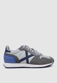 Zapatilla deportiva gris y azul que presenta una combinación de materiales de gamuza y malla, con una suela texturizada y líneas de acento diagonales en los laterales.