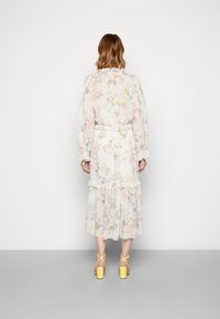 Robe maxi florale en tissu léger, avec de longues manches, taille cintrée, ourlet volanté et couleurs pastel. Associée à des sandales à talons carrés jaunes.