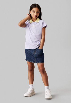 Polo shirt viola chiaro con colletto giallo, gonna mini in denim e sneakers bianche. Il design presenta un logo sul petto e dettagli nella tasca.