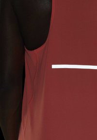 Gros plan d'une personne à la peau foncée portant un maillot de sport rouge sans manches avec une bande blanche horizontale sur le devant.