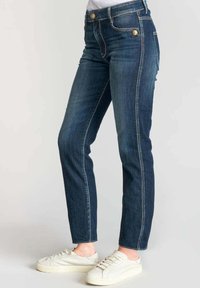 Jeans bleu foncé en denim, avec une coupe slim, un design à cinq poches, des accents en métal doré et des coutures contrastantes.