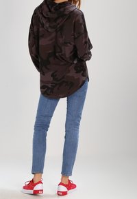 Sudadera de camuflaje negro y gris, de corte relajado, con capucha. Combinada con jeans ajustados de color azul claro y zapatillas rojas de caña baja.