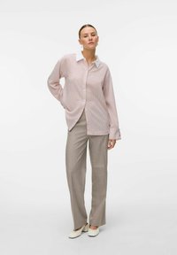 Gestreept lichtroze overhemd met witte kraag, lange mouwen en knoopsluiting, gecombineerd met beige wijde broek en crèmewitte schoenen.