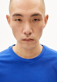 Blaues Rundhals-T-Shirt aus Baumwolle mit kurzen Ärmeln. Der Stoff wirkt glatt und leicht, mit minimalen Nähten und ohne Muster.