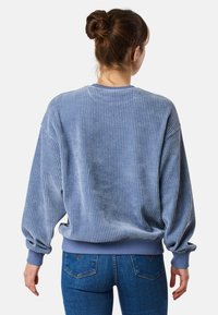 Felpa in velluto a coste azzurro chiaro con texture a coste, scollatura rotonda e maniche con polsini, indossata con jeans blu.