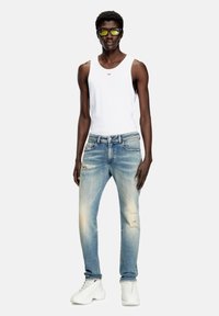 Bela majica na bretele, svetloplave poderane farmerke sa izbljeđenjem, crne sunčane naočare i bele patike. Prilagođen stil sa vidljivim šavovima i džepovima.