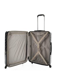 Maleta rígida con un exterior negro que presenta un estampado floral, un interior beige, un mango retráctil y correas interiores para asegurar los objetos.