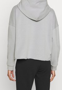 Felpa grigia chiara, taglio cropped, con una texture morbida, vestibilità oversize e orlo grezzo; presenta un ampio cappuccio e spalle scese. Abbinata a pantaloni neri.