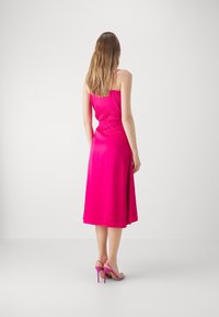 Fuksia satindress med en tettsittende bodice, elastisk midje og en A-linje silhuett, komplementert med høyhælte rosa sandaler.