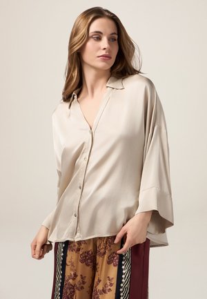 Blusa di seta beige chiaro con colletto, design morbido e maniche a tre quarti. Presenta bottoni discreti e una texture liscia.
