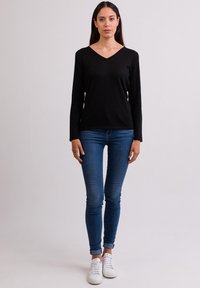 Schwarzes langärmliges V-Ausschnitt-Oberteil, kombiniert mit blauen Skinny-Jeans und weißen Sneakers. Das Oberteil hat ein schlichtes Design und eine weiche Textur.