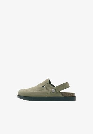 Sandalo slip-on in camoscio verde oliva con cinturino posteriore regolabile e suola nera, vista laterale su sfondo bianco.