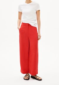 Röda vida byxor med texturerad yta, med framfickor och slät front. Kombinerat med en figurnära vit kortärmad skjorta och svarta sandaler.