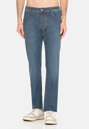 Jeans in denim blu con una vestibilità dritta, caratterizzati da cuciture arancioni, chiusura frontale con bottone e due tasche laterali. Indossati con sneaker di colore chiaro.
